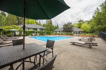 A pool area with a table and chairs and a green umbrella.